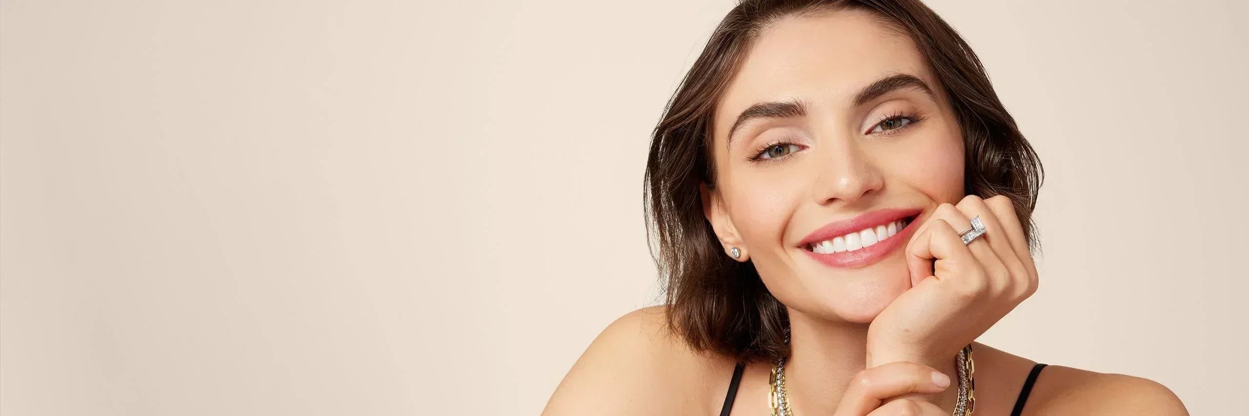 Smiling woman wearing silver earrings, gold-plated chain necklace, and stacked rings
