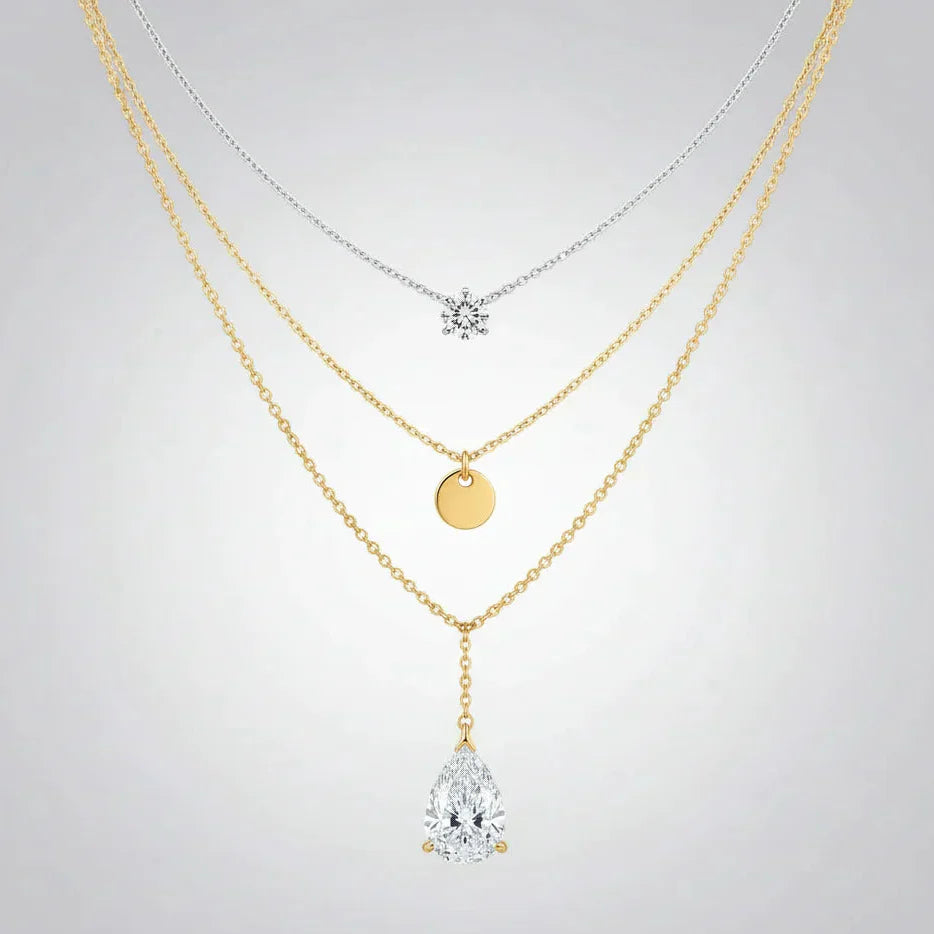 Layered gold and silver necklaces featuring a snowflake, gold disc, and teardrop pendant on a white background