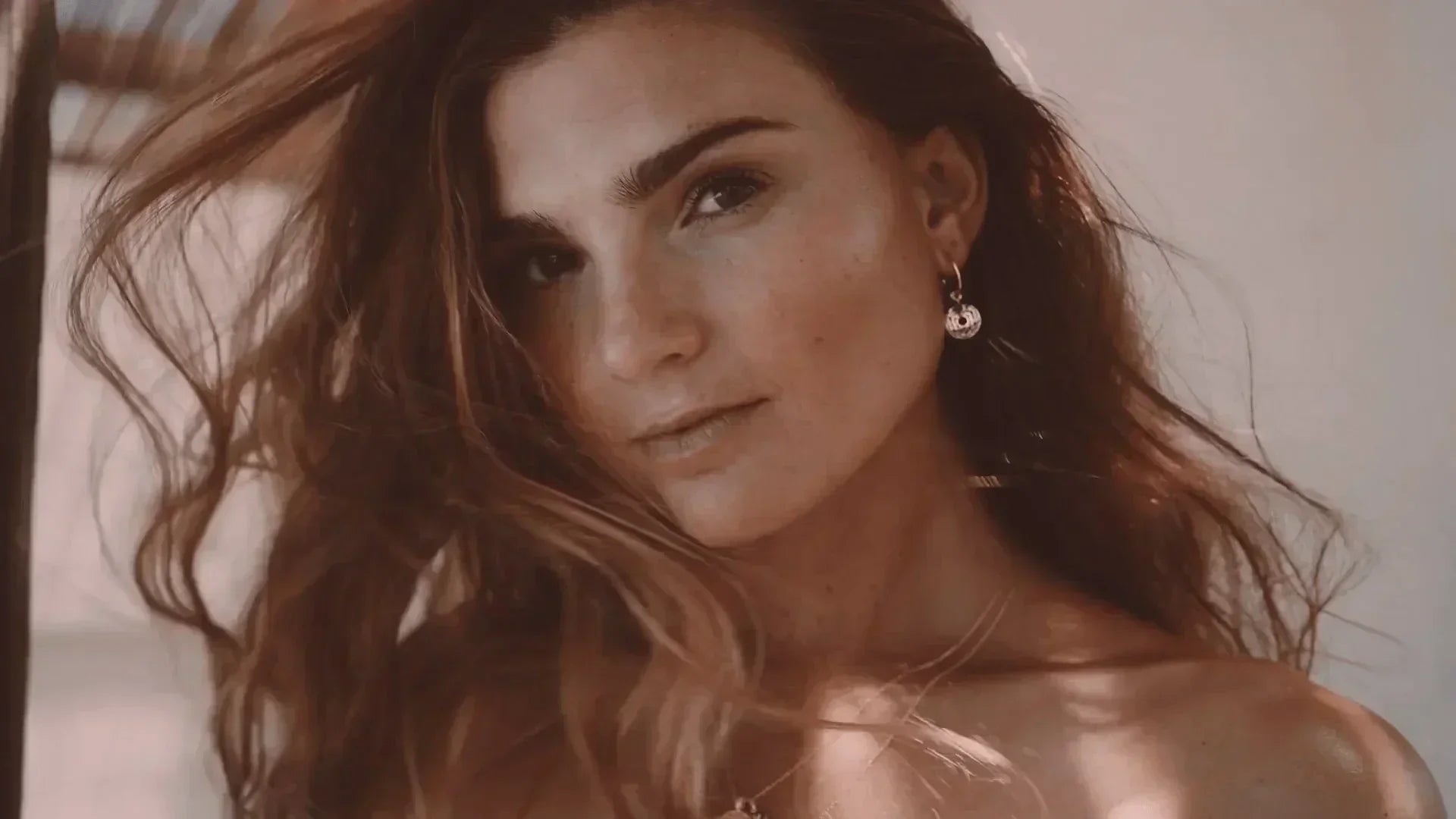 Woman with wavy brown hair wearing silver hoop earrings and delicate necklace, close-up