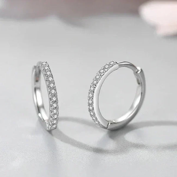 Pair of silver hoop earrings with clear stones on a light gray background