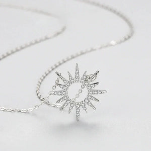 Silver sun-shaped pendant on a chain against a light gray background