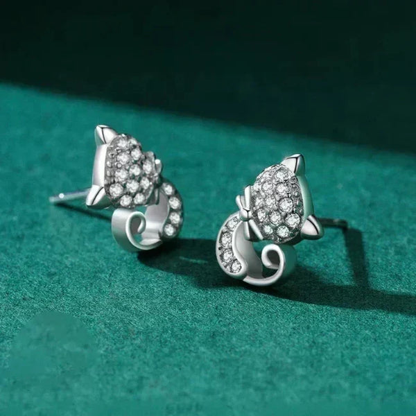 Silver cat-shaped earrings with gemstones on a green textured surface