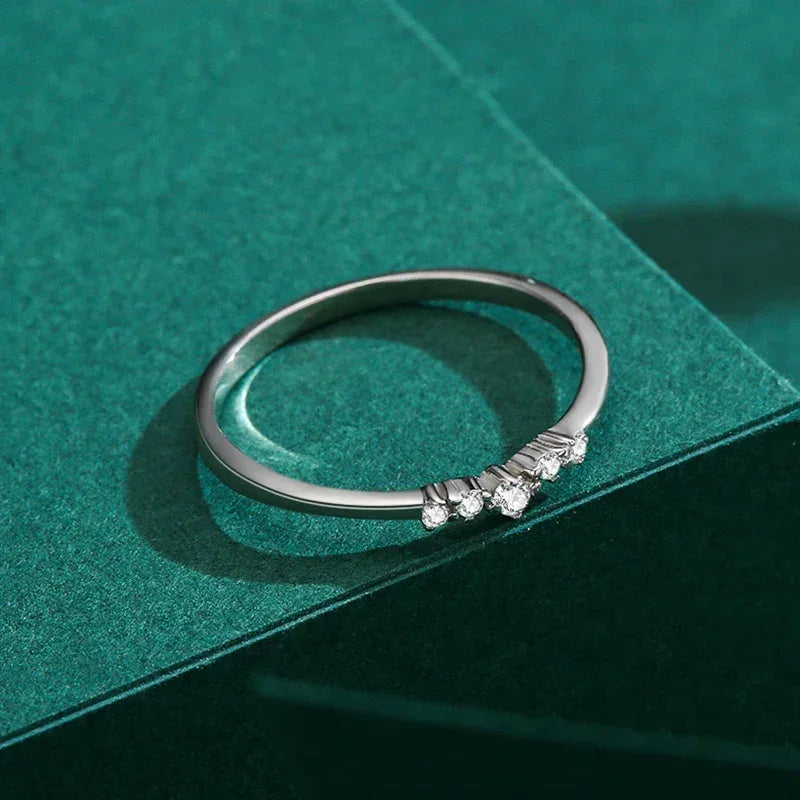 Delicate silver ring with small white gemstones on green background, elegant minimalist jewelry