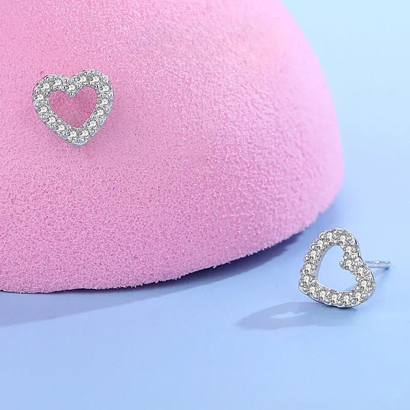Sterling silver heart stud earrings with sparkling crystals on a pastel pink and blue background