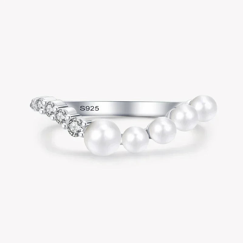 Sterling silver ring with white pearls and small clear gemstones on plain background