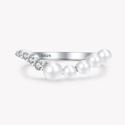 Sterling silver ring with white pearls and small clear gemstones on plain background