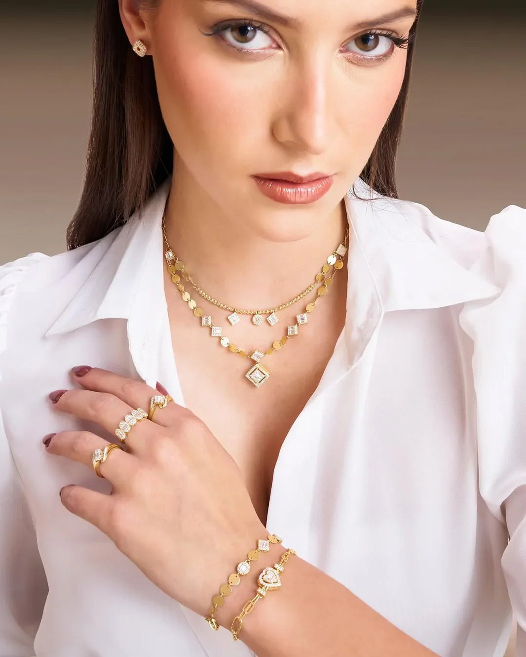 Woman wearing gold jewelry including a necklace, bracelet, and ring on a neutral background
