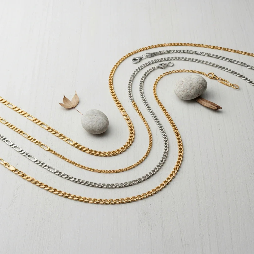 Gold and silver chain necklaces on a light wooden surface with stones and leaves.