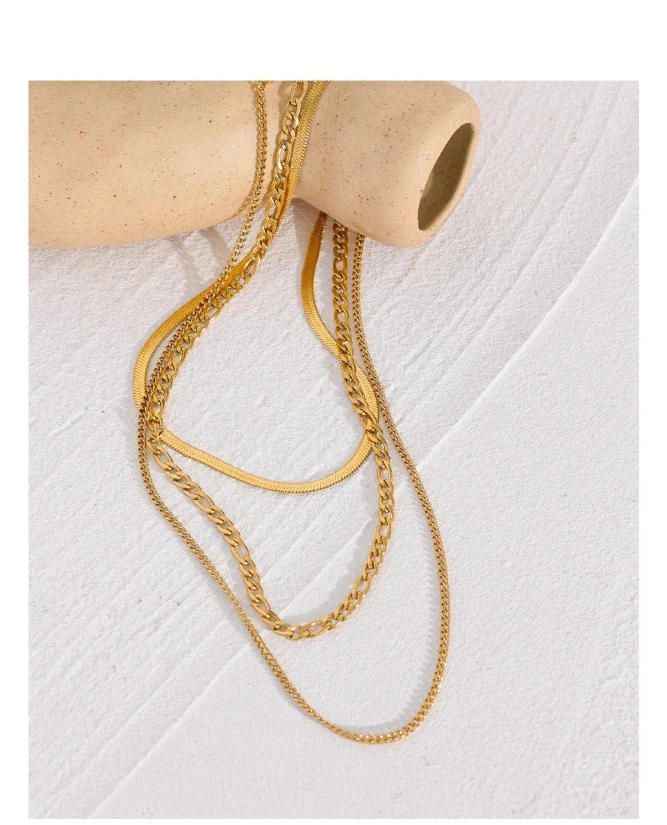 Layered gold-plated chain necklaces displayed on a neutral ceramic prop, textured background