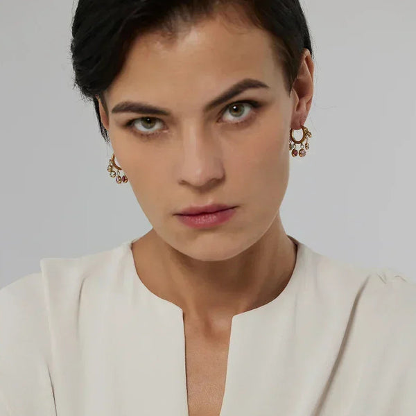Woman wearing gold-plated dangle earrings with gemstones, cream blouse, neutral background