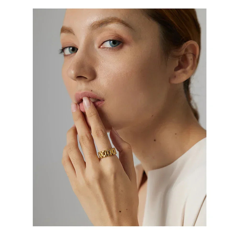 Woman wearing a chunky gold-plated chain ring, touching her lips, elegant neutral background