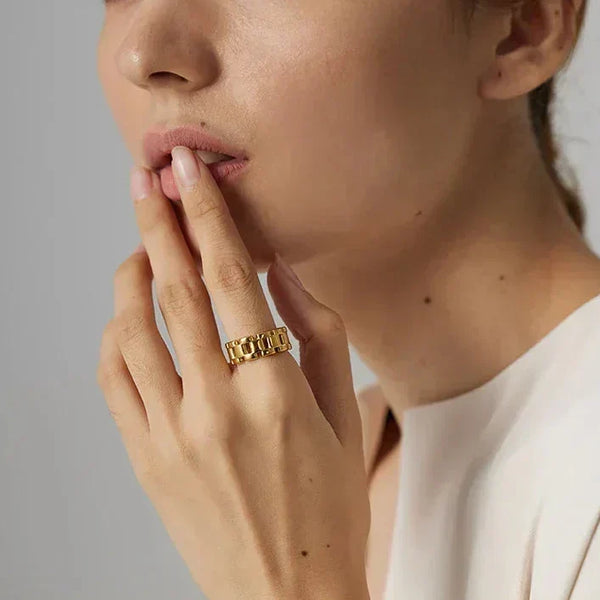 Woman wearing a chunky gold-plated chain ring, touching her lips, elegant neutral background