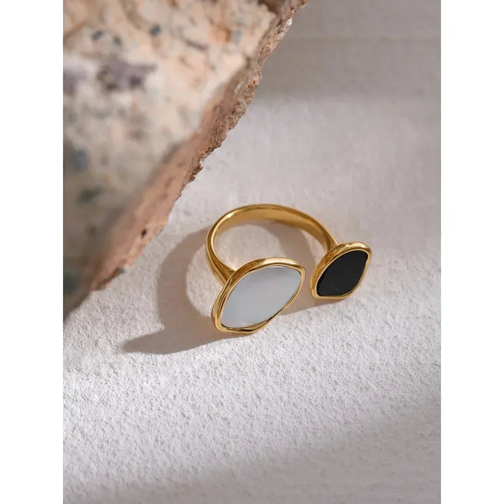 Gold-plated open ring with black and white stones on textured surface