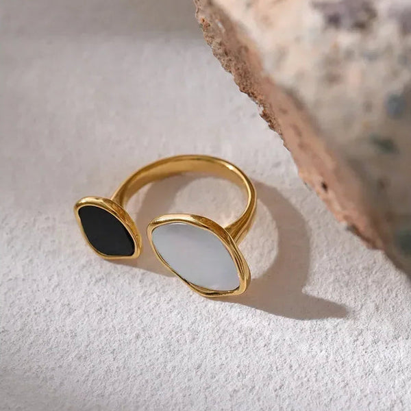 Gold-plated open ring with black and white stones on textured surface