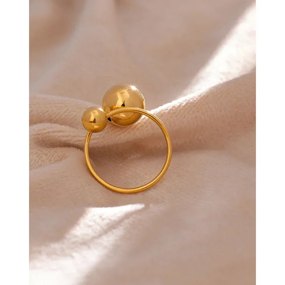 18K gold-plated ring with two polished spheres on a soft beige fabric background