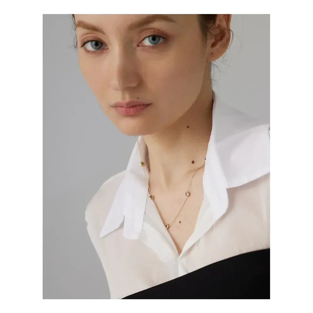 Woman wearing delicate 18K gold-plated necklace with gemstone accents, white collared shirt