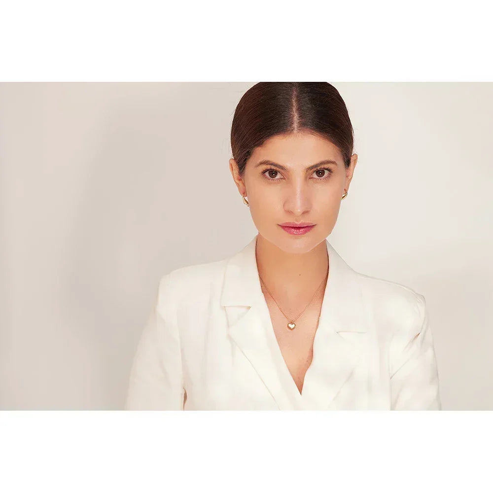 Woman wearing 18K gold-plated heart necklace and matching hoop earrings, white blazer
