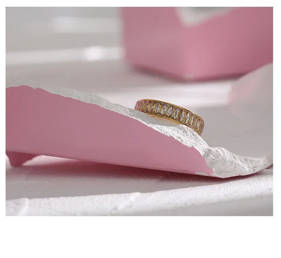 Gold-plated ring with baguette-cut crystals on a pink and white textured surface