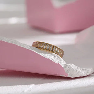 Gold-plated ring with baguette-cut crystals on a pink and white textured surface