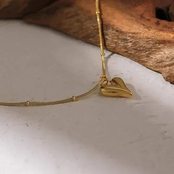 Gold-plated heart pendant necklace on wood and white background, elegant women's jewelry