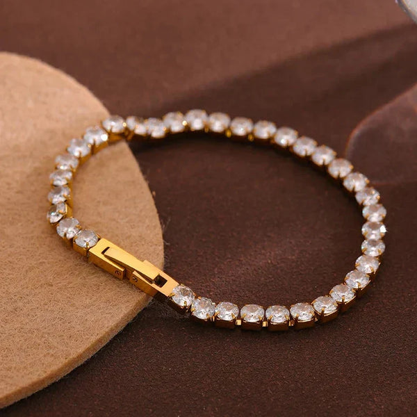 Gold bracelet with clear stones on a brown surface, featuring the 'Vogue' brand.