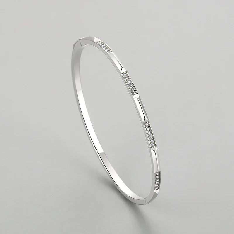 Sterling silver bangle with geometric segments and small embedded crystals on plain background