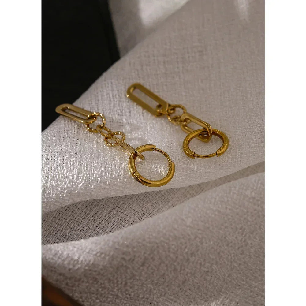 Pair of gold-plated hoop earrings with geometric links on a textured white fabric background