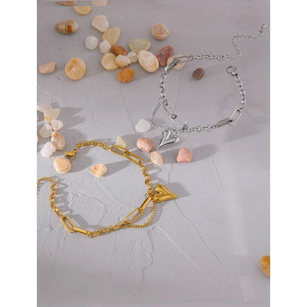 Gold and silver heart charm chain bracelets on a textured surface with small stones