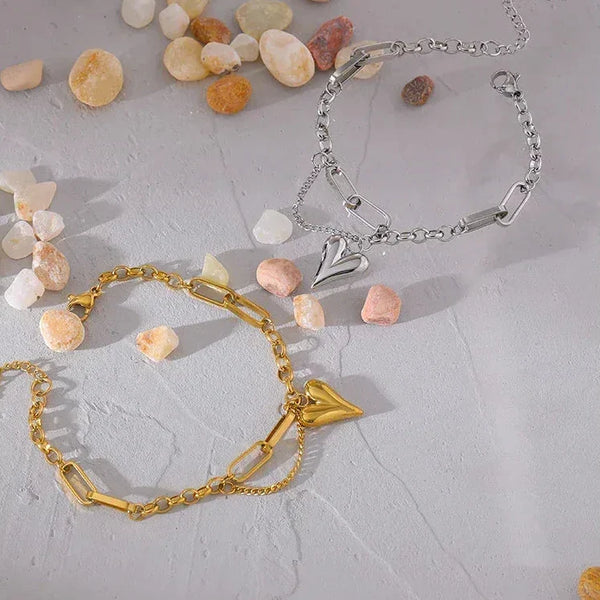 Gold and silver heart charm chain bracelets on a textured surface with small stones
