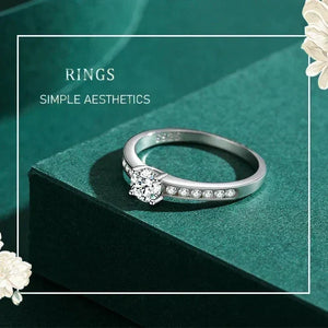 Silver ring with small diamonds on a green surface with white flowers.
