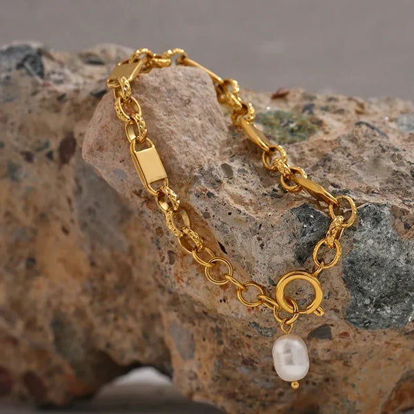 Gold bracelet with a pearl charm on a textured stone surface