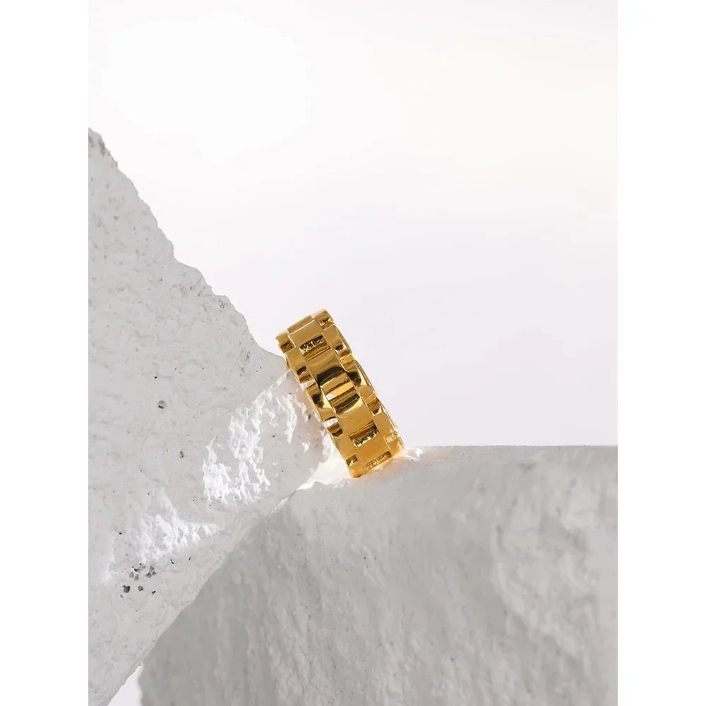Chunky gold-plated chain ring displayed on textured white stone, modern jewelry design