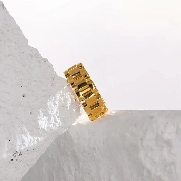 Chunky gold-plated chain ring displayed on textured white stone, modern jewelry design