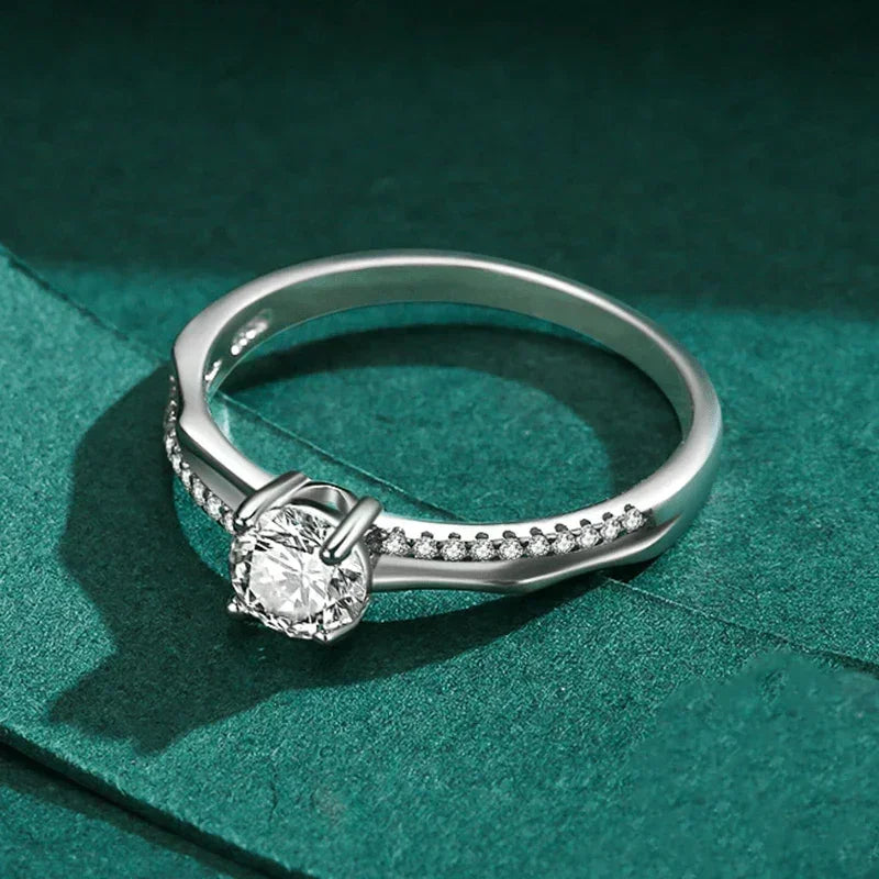 Sterling silver engagement ring with round solitaire and pavé stones on green background