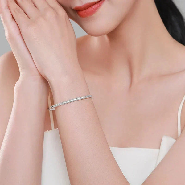 Woman wearing a silver bracelet on a neutral background.