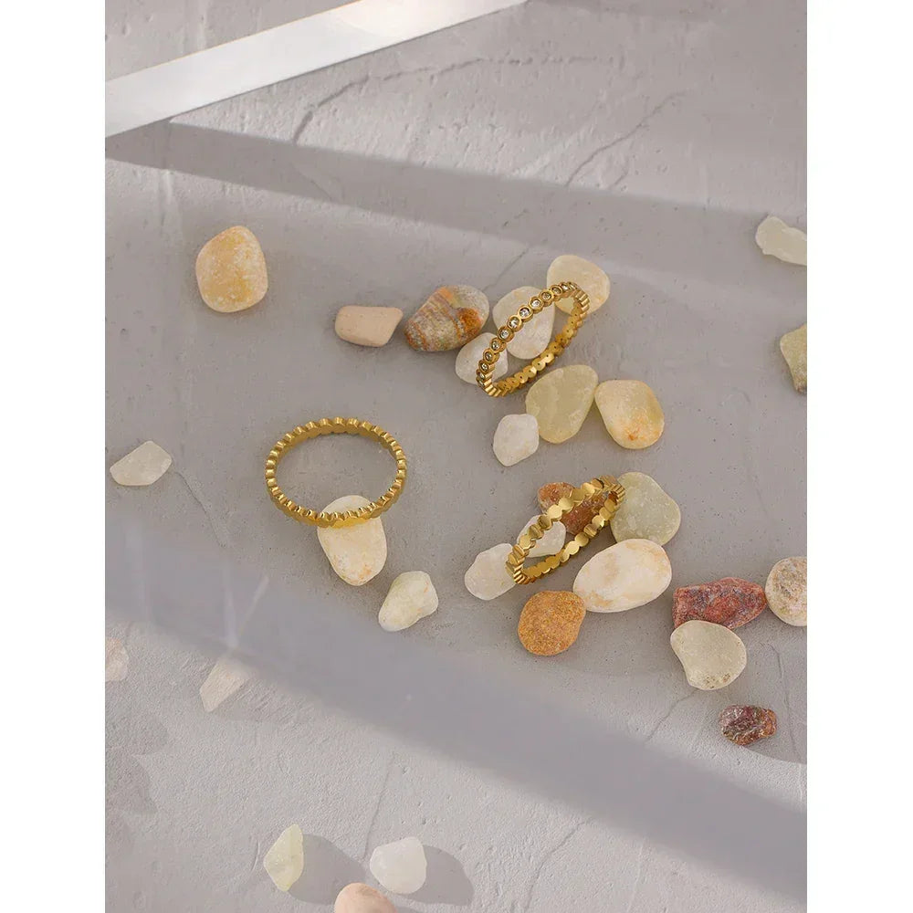 Gold-plated textured stacking rings displayed on smooth stone pebbles and concrete.