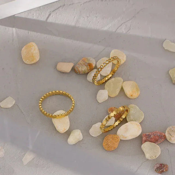 Gold-plated textured stacking rings displayed on smooth stone pebbles and concrete.