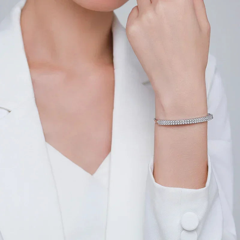 Woman wearing a silver tennis bracelet with sparkling stones, styled with a white blazer.