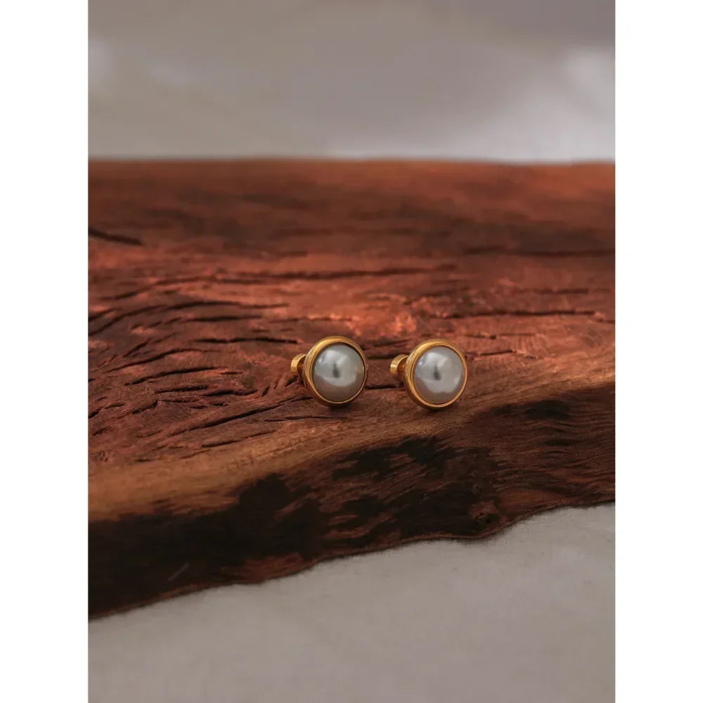 Pair of gold-plated pearl stud earrings on rustic wood surface