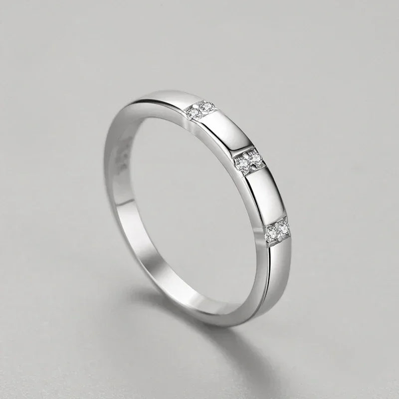 Sterling silver band ring with three sections of small clear gemstones on a gray background
