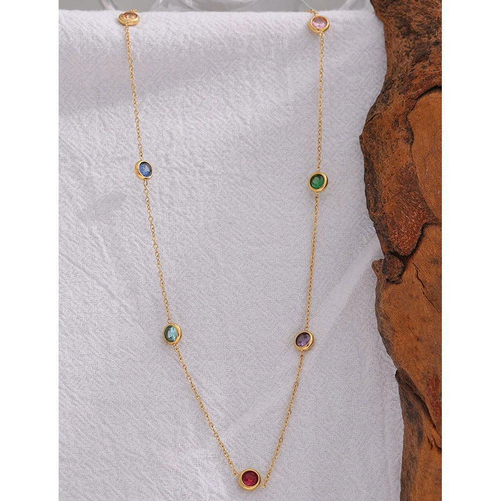 18K gold-plated necklace with multicolored gemstone stations on a white textured background