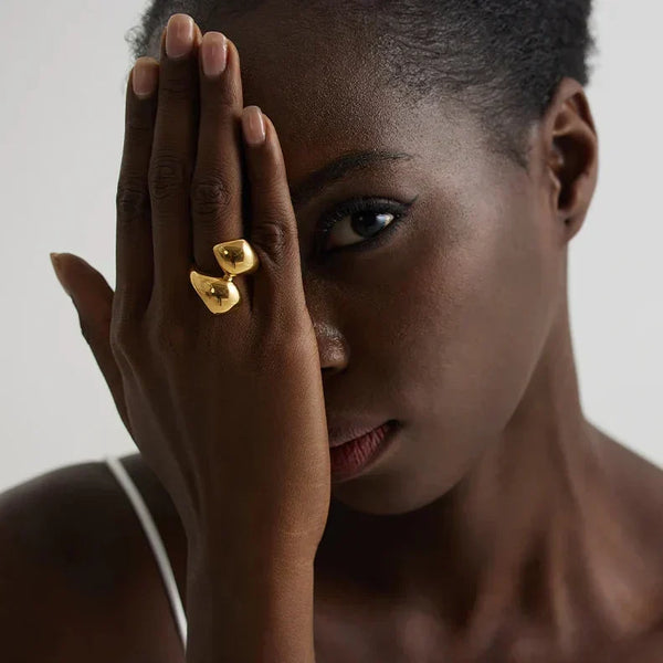 Woman wearing unique gold-plated statement ring on hand, in white pleated dress