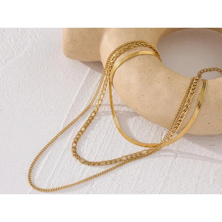 Layered gold-plated chain necklaces displayed on a textured cream ceramic ring