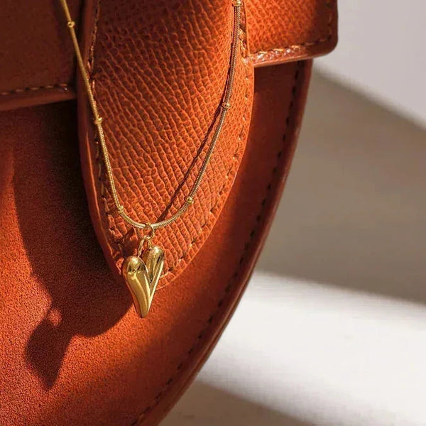 Gold-plated heart pendant necklace on textured brown leather bag in sunlight