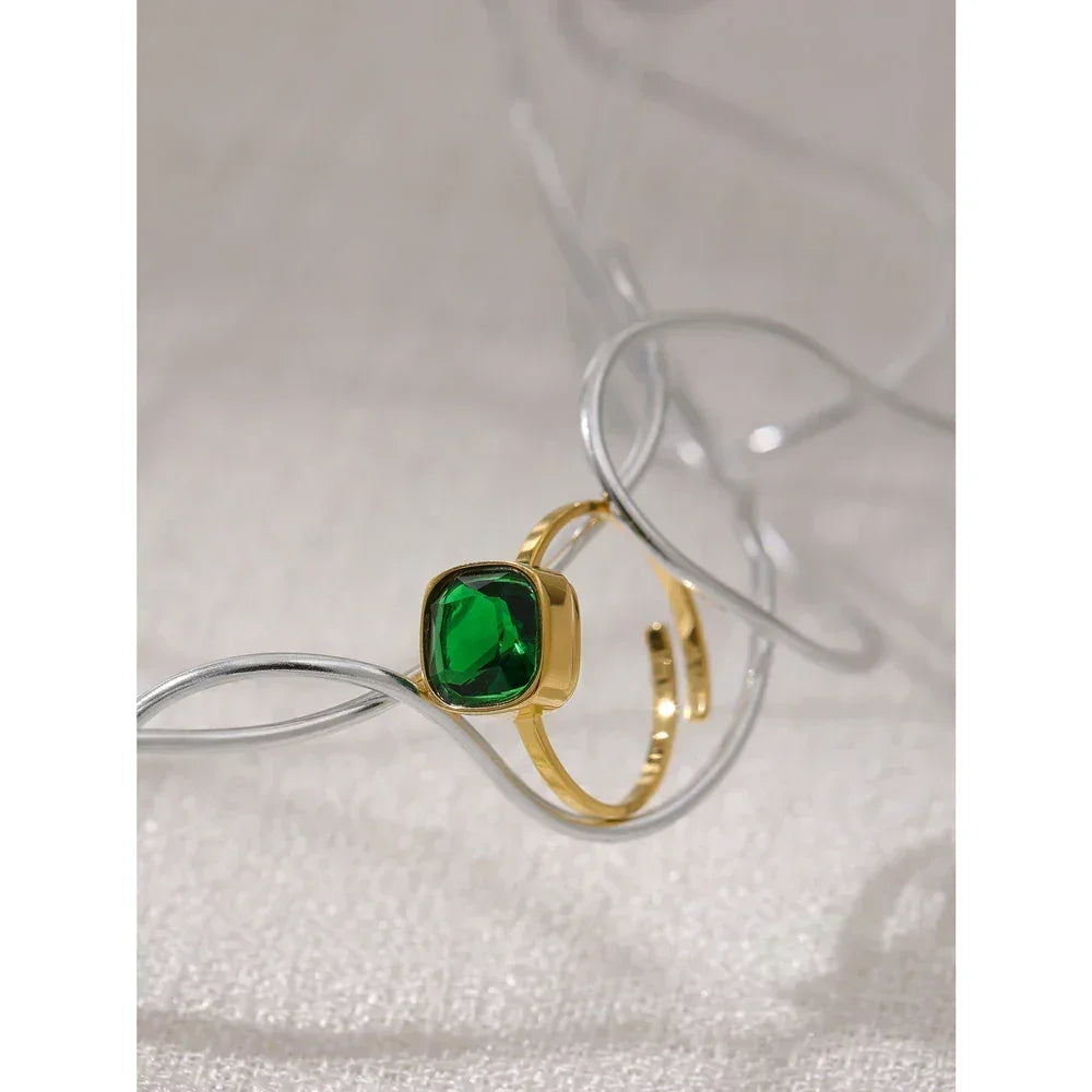 Gold-plated ring with square green gemstone displayed on textured surface
