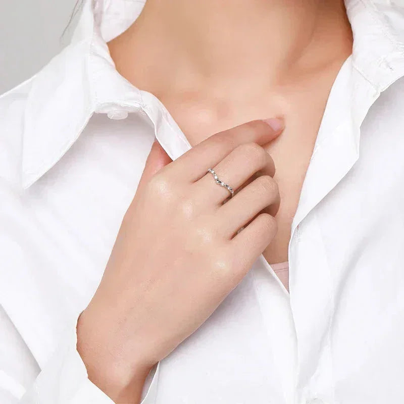 Woman wearing a delicate 925 silver ring with small stones on her finger, white blouse