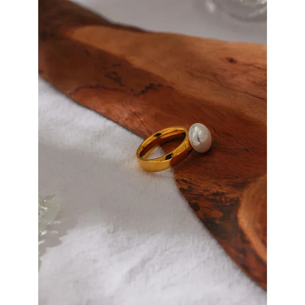 Gold-plated ring with a large white pearl on a wooden surface, elegant jewelry