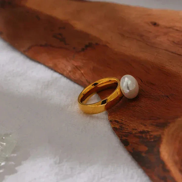 Gold-plated ring with a large white pearl on a wooden surface, elegant jewelry