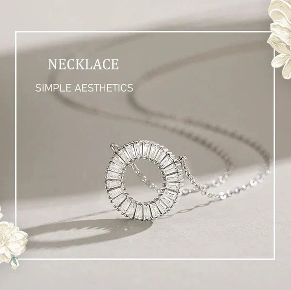 Silver necklace with a circular pendant on a light background, surrounded by white flowers.