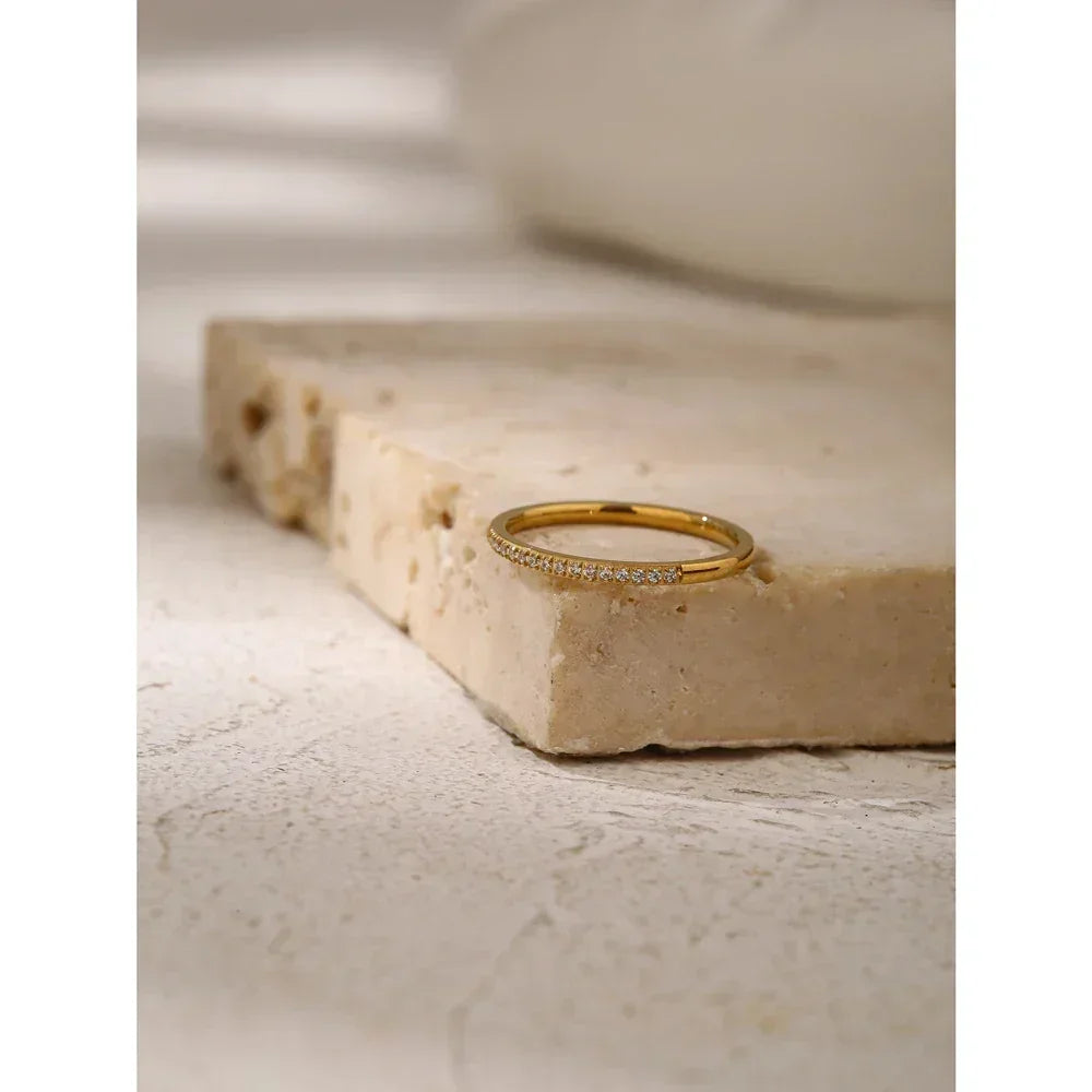 Gold-plated thin ring with small clear stones on textured stone surface